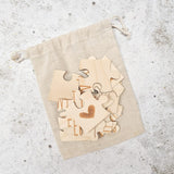 Losse houten puzzelstukjes met letters en een hartje op een beige linnen zakje.