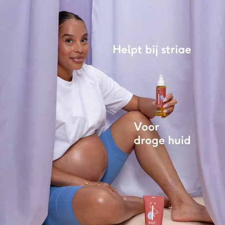 Zwangere vrouw zit tussen lila gordijnen met een flesje Naïf Relaxing Body Oil in haar hand.