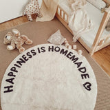 Rond crèmekleurig tapijt met zwarte tekst 'Happiness is Homemade' en hartje naast een kinderbed en knuffelbeer.
