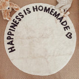 Rond crèmekleurig tapijt 'Happiness is Homemade' van bovenaf, met zwart hartje, knuffelbeer en houten blokken.