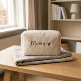 Crèmekleurige Teddy toilettas met bruin opschrift 'Mama' en hartje, op gevouwen stof op een houten tafel.