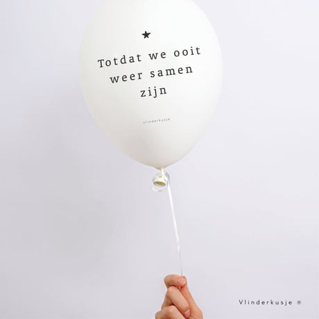 Witte troostballon met zwart sterretje en de tekst ‘Totdat we ooit weer samen zijn’, aan een lint vastgehouden.