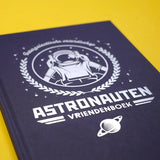 Detail van de donkerblauwe kaft van het astronautenvriendenboek met witte astronaut, sterren en planeet.