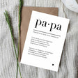 Witte ansichtkaart Papa met zwarte tekst en een klein hartje, op een bruine envelop naast groene takjes.