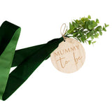 Donkergroene fluwelen buiksjerp met ronde houten badge ‘Mummy to be’ en groene blaadjes op een witte achtergrond.
