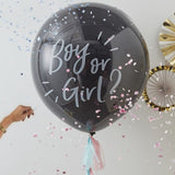 Zwarte gender reveal ballon met tekst ‘Boy or Girl?’, omringd door roze en blauwe confetti, met een hand ernaast