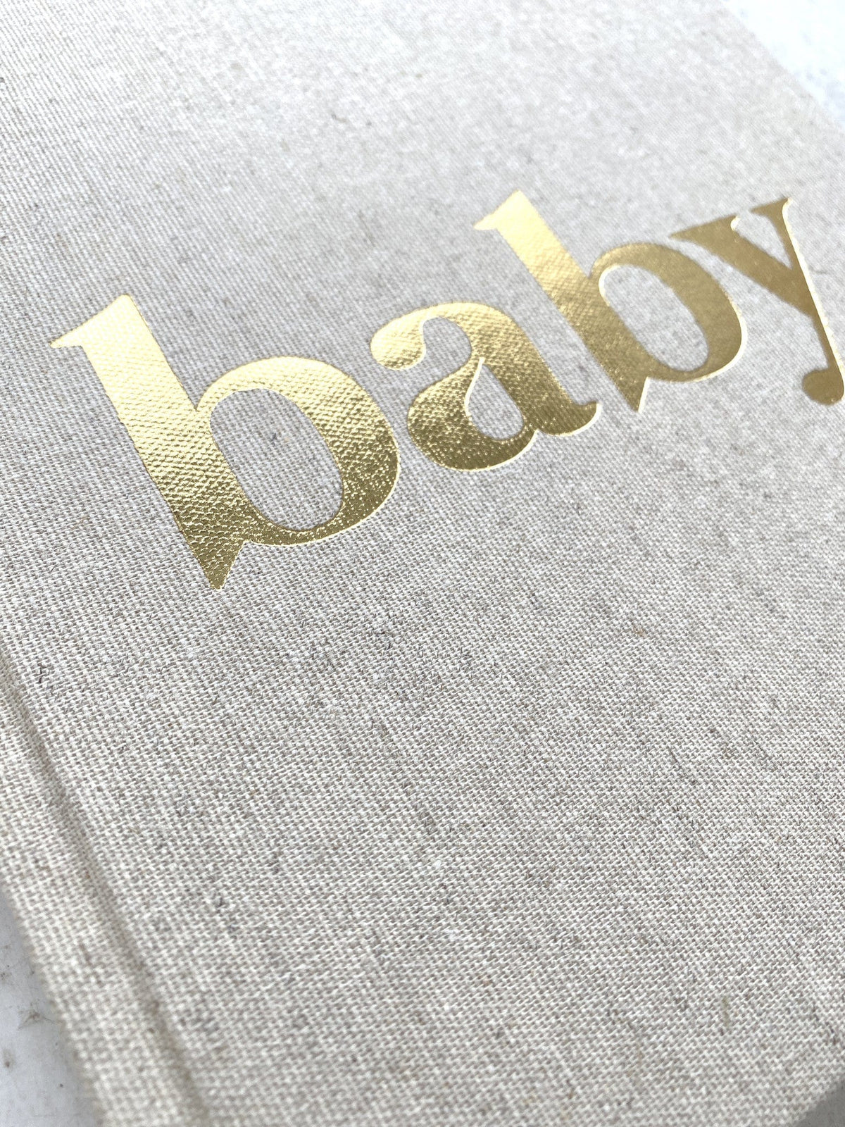 Detail van de linnen kaft van het baby-invulboek met glanzende goudfolieletters ‘baby’.