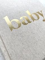 Detail van de linnen kaft van het baby-invulboek met glanzende goudfolieletters ‘baby’.