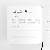Opengeslagen zwangerschapsdagboek met invulpagina voor 18 weken, zwarte tekst, hartjes en een zwart leeslint.