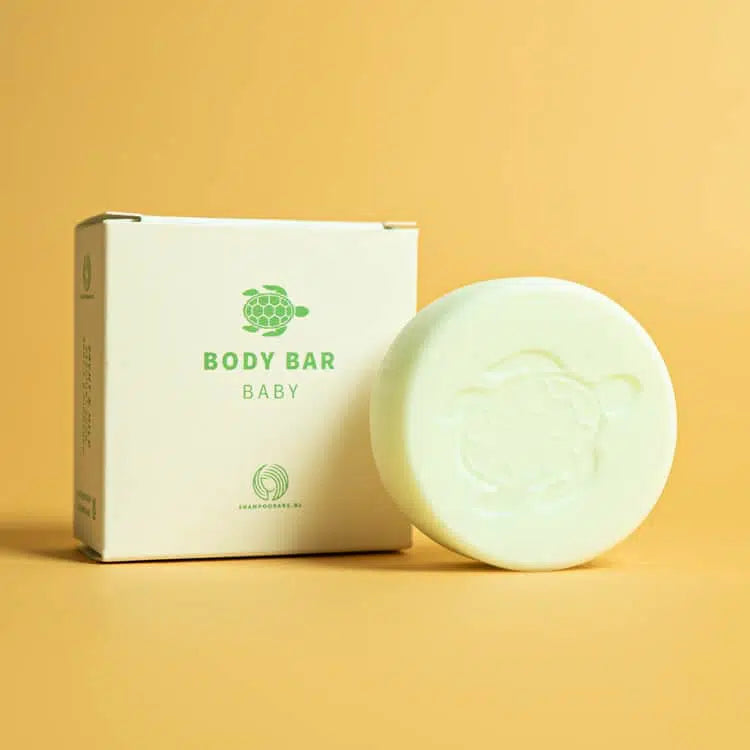 Ronde baby body bar met schildpadreliëf naast het doosje op een gele achtergrond