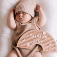 Houten regenboogletterbord met 'rainbow baby', bloemen en maantjes op de buik van een slapende baby.