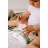 Baby in een wit rompertje met een geopend pak Naïf plasticvrije billendoekjes tussen de benen.