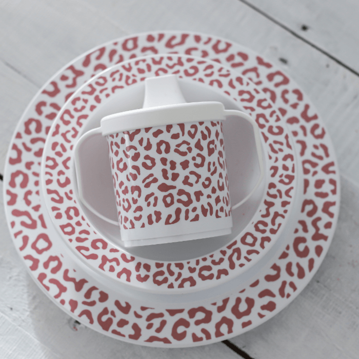 Servies Leopard Blush met oudroze luipaardprint, gestapeld op een witte houten tafel.