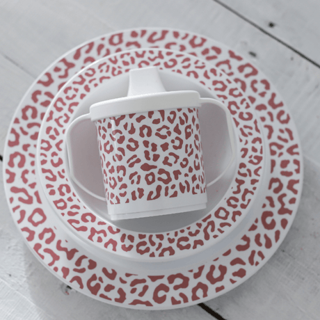 Servies Leopard Blush met oudroze luipaardprint, gestapeld op een witte houten tafel.