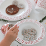 Kinderhand met een koekje naast een witte kom Leopard Blush met oudroze luipaardprint en koekjes.