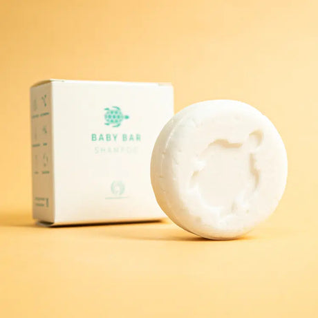 Witte, ronde Shampoo Bar Baby met schildpadmotief naast de verpakking op een gele ondergrond.