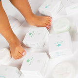 Kindervoetjes tussen witte Shampoo Bar Baby-verpakkingen en ronde shampoobars met schildpadmotief.