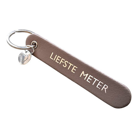 Taupe sleutelhanger met de tekst 'Liefste meter', een zilverkleurige sleutelring en hartbedel.