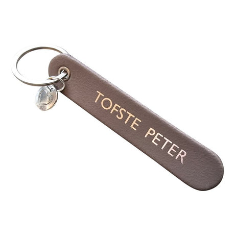 Taupe sleutelhanger met opdruk 'Tofste peter', zilverkleurige sleutelring en hartbedel.