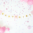 Baby Girl-slinger met witte en roze vlaggetjes, gouden letters en een hartje, tussen roze ballonnen en confetti.