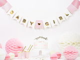 Baby Girl-slinger met gouden letters en roze vlaggetjes boven een taarttafel met roze en witte decoratie.