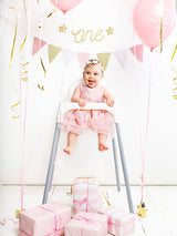 Roze slinger boven een baby in een kinderstoel, tussen roze ballonnen en cadeautjes.