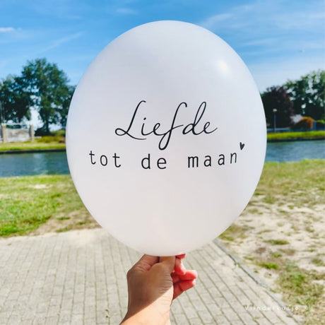 Witte troostballon met de tekst 'Liefde tot de maan', vastgehouden met één hand bij het water.