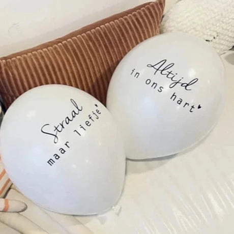 Witte troostballonnen met de teksten 'Straal maar liefje' en 'Altijd in ons hart' op een bank.