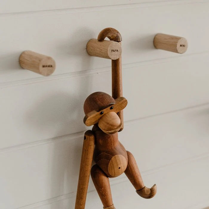 Drie houten Family-wandhaken aan een witte wand, met een houten aap aan de haak met opschrift Papa.